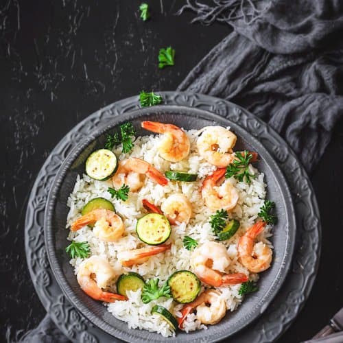 Italian risotto with shrimp and zucchini on a gray plate with black background.