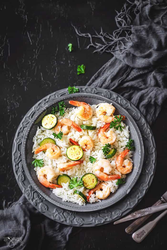 Italian risotto with shrimp and zucchini on a gray plate with black background. 