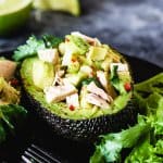 Half of avocado skin with tuna salad on a black plate and forks.
