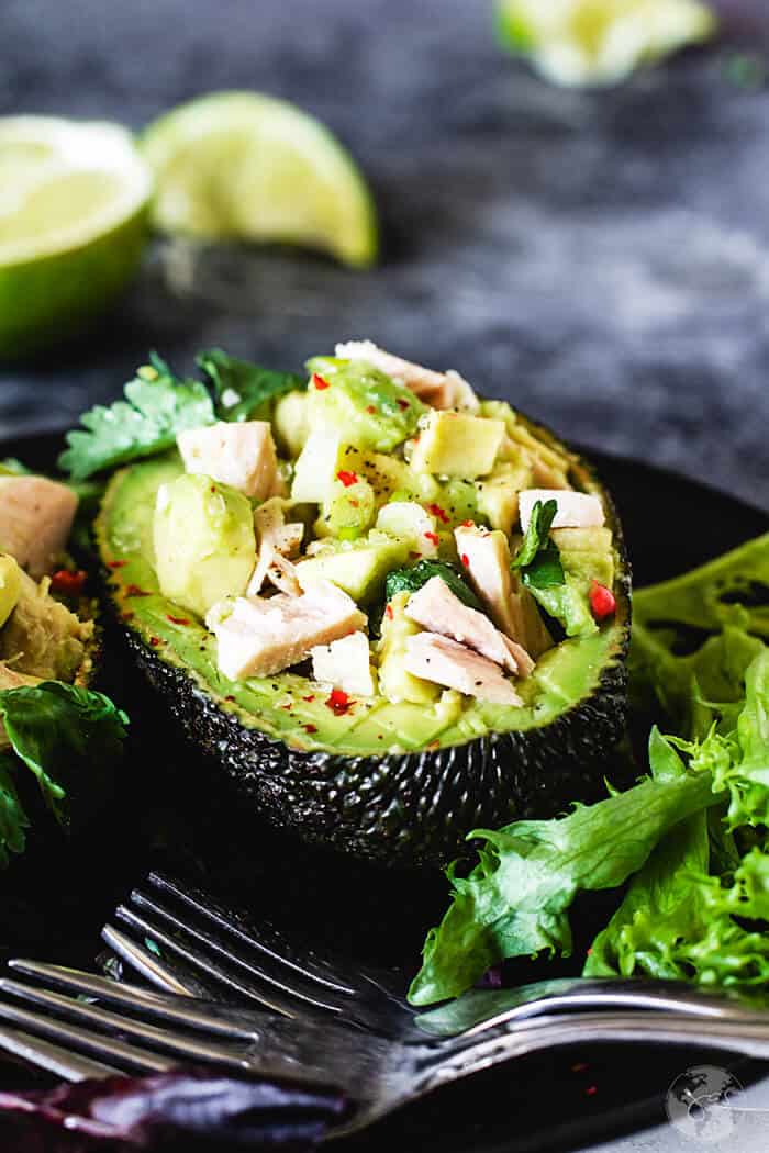 Half of avocado skin with tuna salad on a black plate and forks.