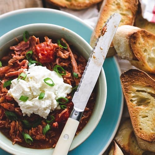 A bowl with the pulled pork gravy on a plate, with ricotta and toasted bread.