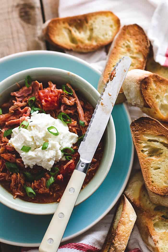 A bowl with the pulled pork gravy on a plate, with ricotta and toasted bread.