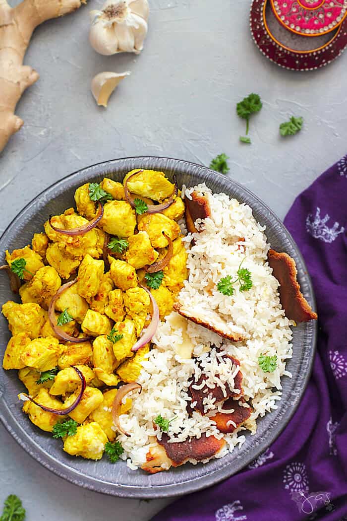 A flat lay of the chicken dish and rice in a shallow bowl with ginger and garlic around it.