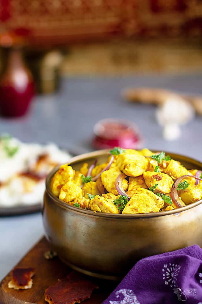 A front shot of a copper bowl with Indian dish with rice and small in the background