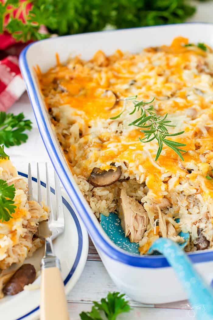 A white casserole dish with cheesy rice and turkey meat with a serving spoon