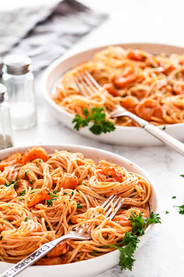 A shot of two plates with shrimp and pasta on a white background