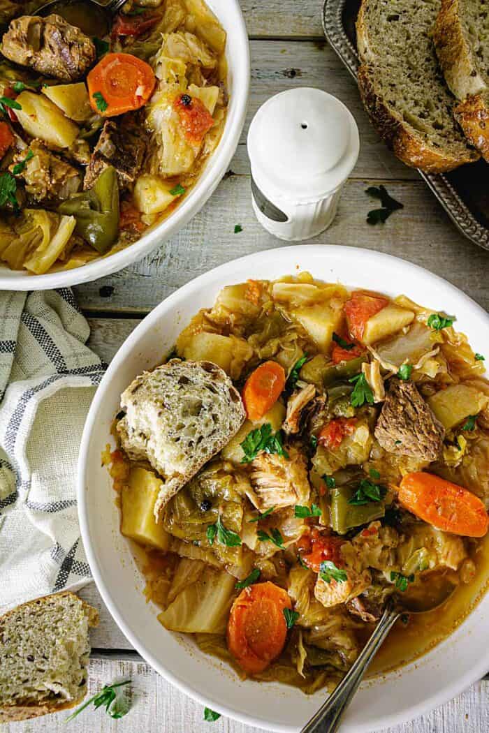 Two white plates of cabbage stew on a wooden surface.