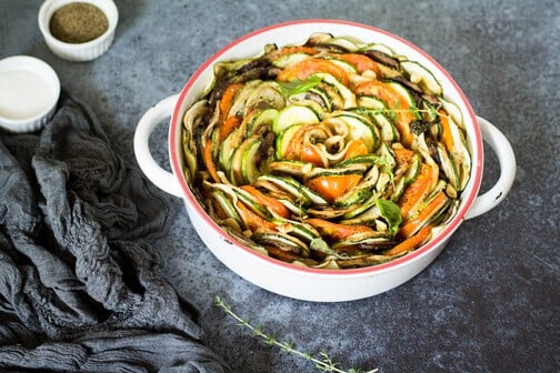 A bowl of sliced vegetables, with eggplant, tomato, and zucchini