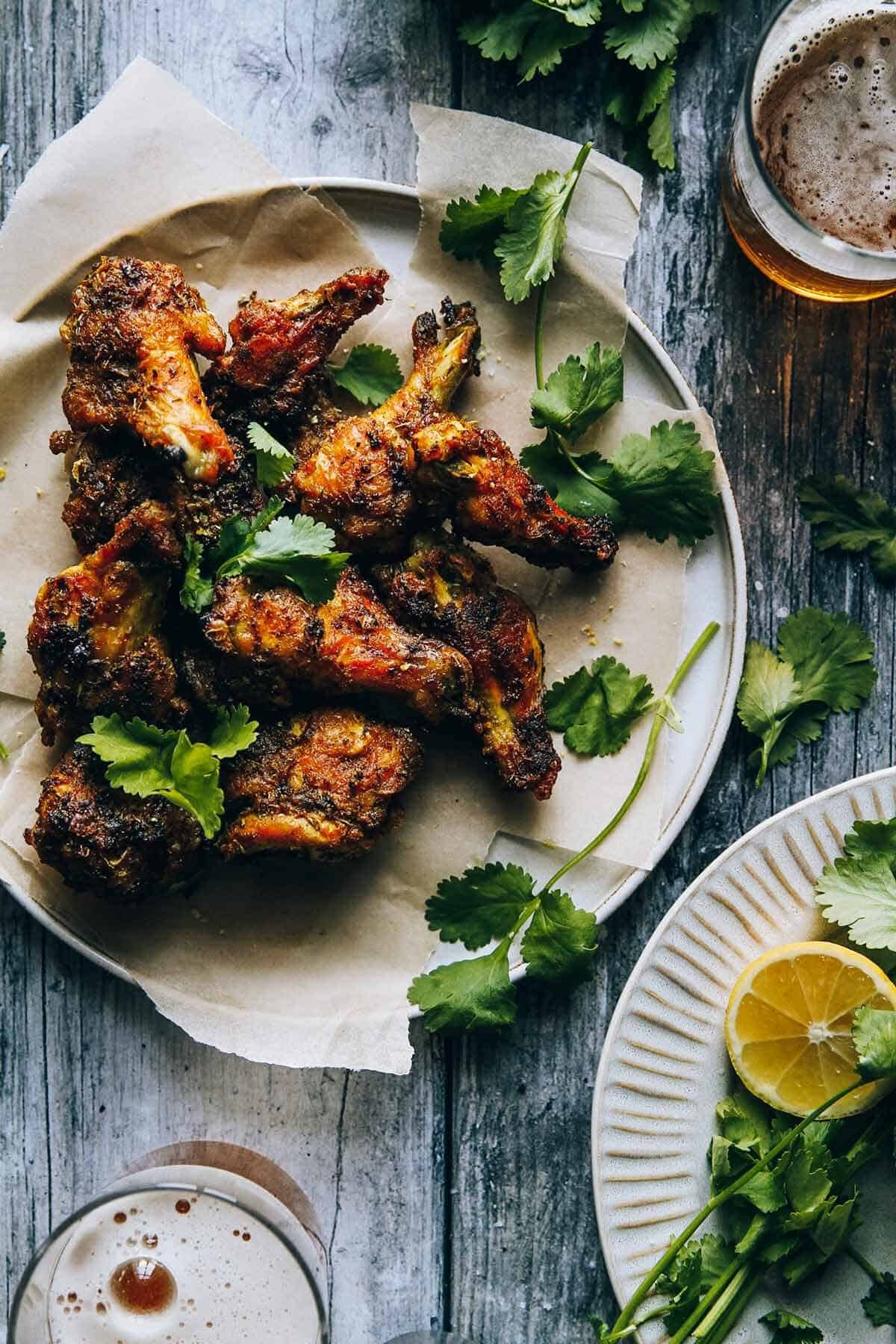 A flat lay of chicken wings on a plate sitting on a table with beer glasses.