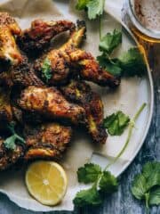 Close up of the crispy wings on a plate with cilantro and lemon.