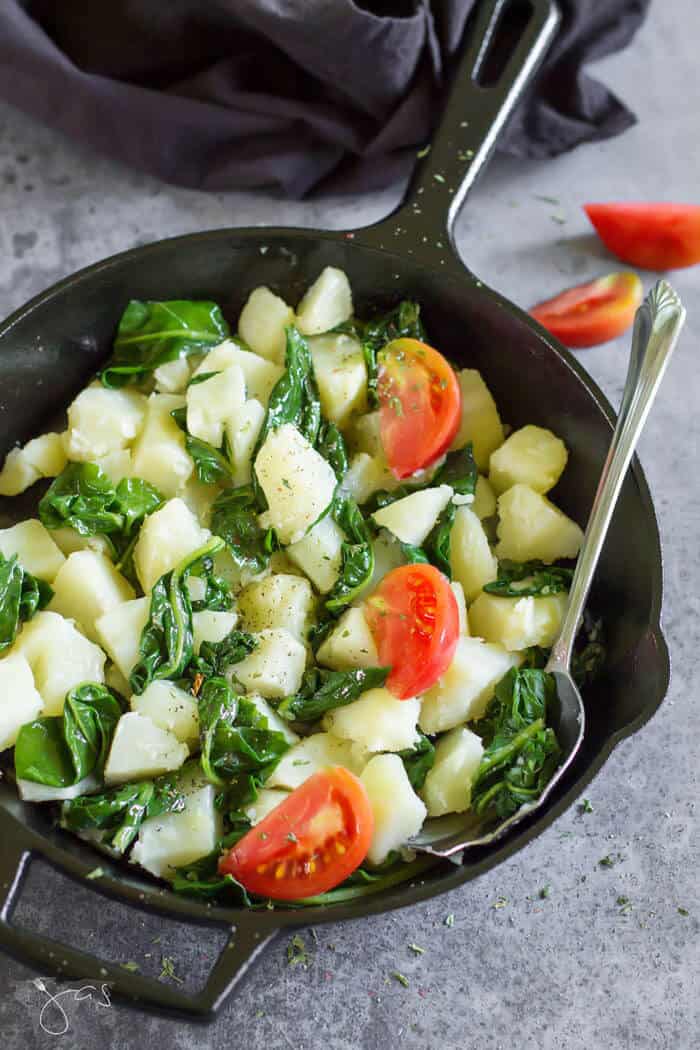 A cast-iron skillet with potatoes, Swiss chard, and tomatoes.