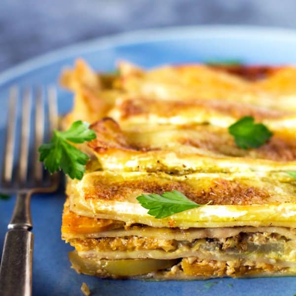 A slice of apple butternut squash lasagna on a blue plate with blue background.