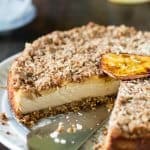 A whole apple oatmeal cheesecake on a plate with one slice removed