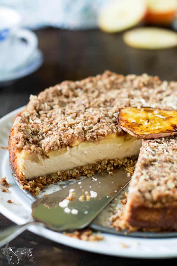 A whole apple oatmeal cheesecake on a plate with one slice removed