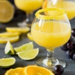 Three glasses with drink on a table with orange and lime slices and grapes