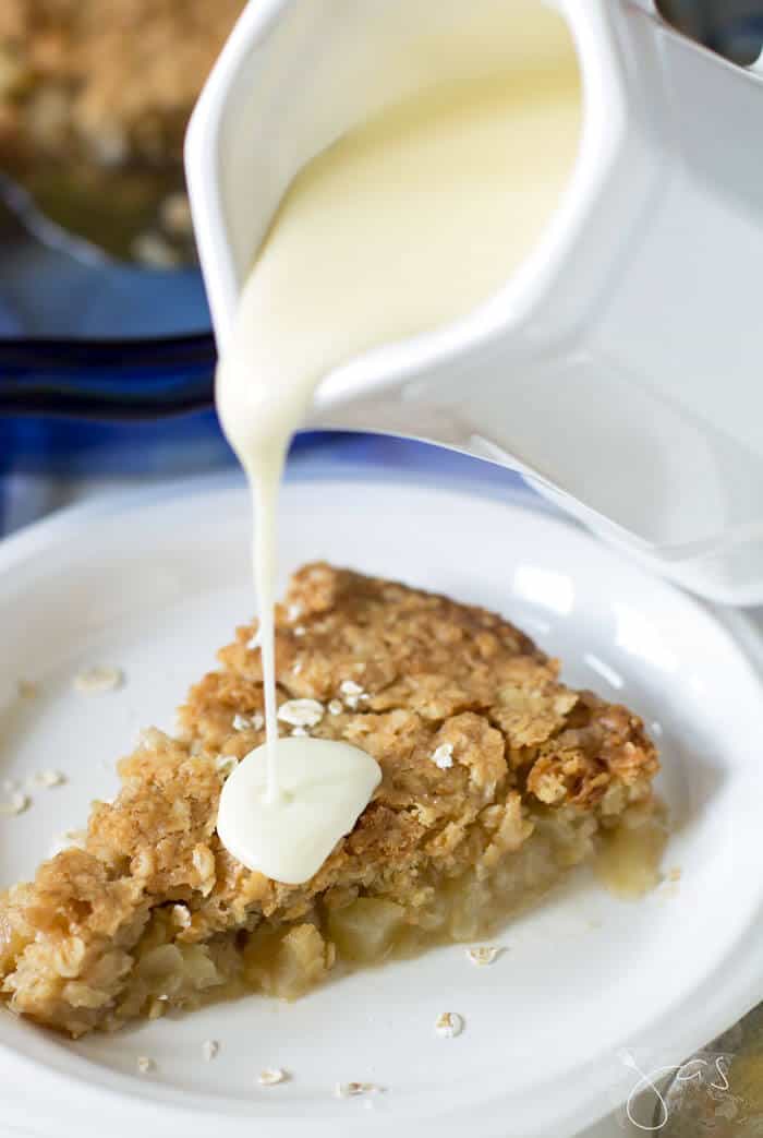 Homemade vanilla sauce being poured over warm apple pie.