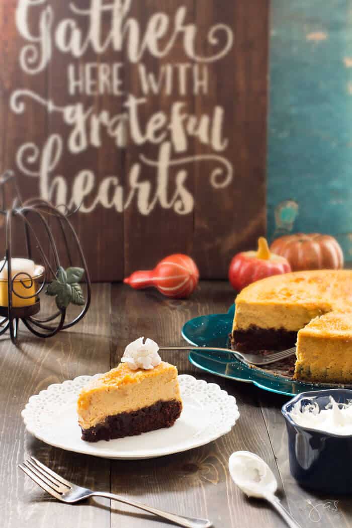 A slice of pumkin cheesecake on a white plate with Thanksgiving decoration in the background