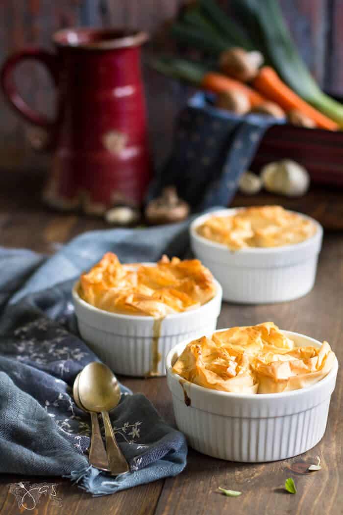 Individual pot pies with vegetables on a table with spoons.