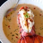 A close up of salmon bisque and lobster tail in a bowl with spoon