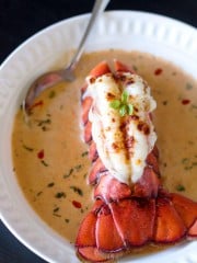 A close up of salmon bisque and lobster tail in a bowl with spoon