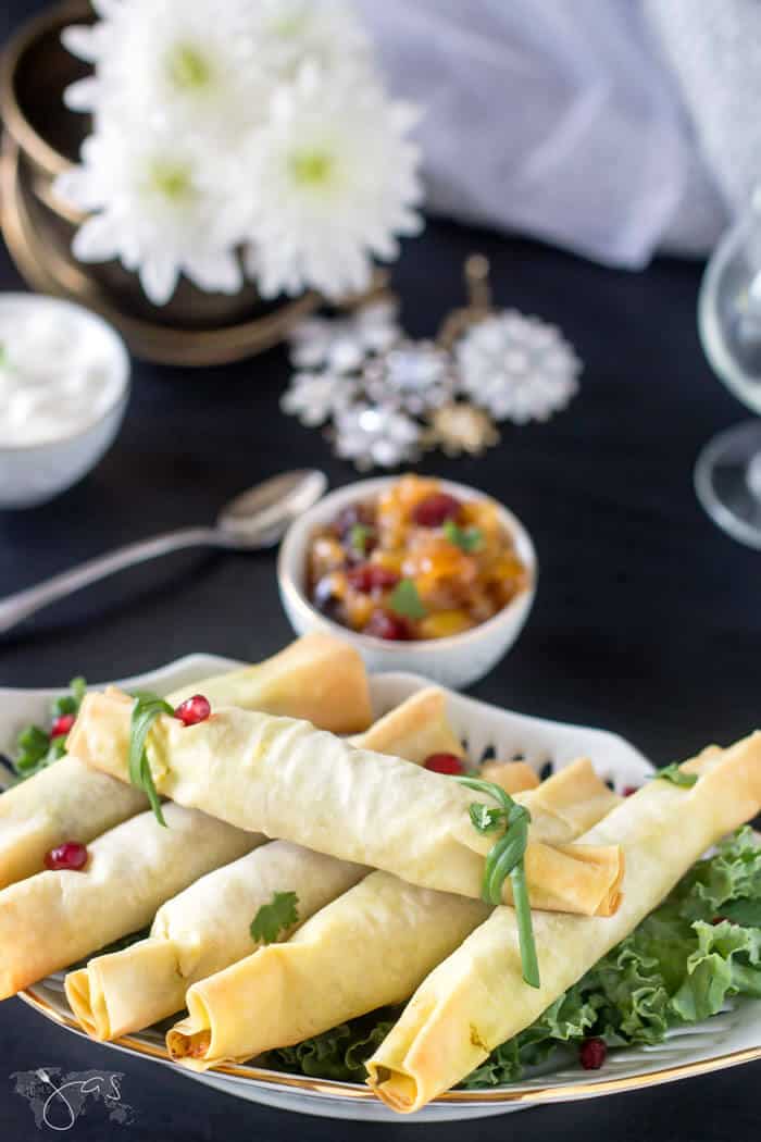 Fillo dough stuffed with spicy samosa on a plate sitting on the table with flowers and other food