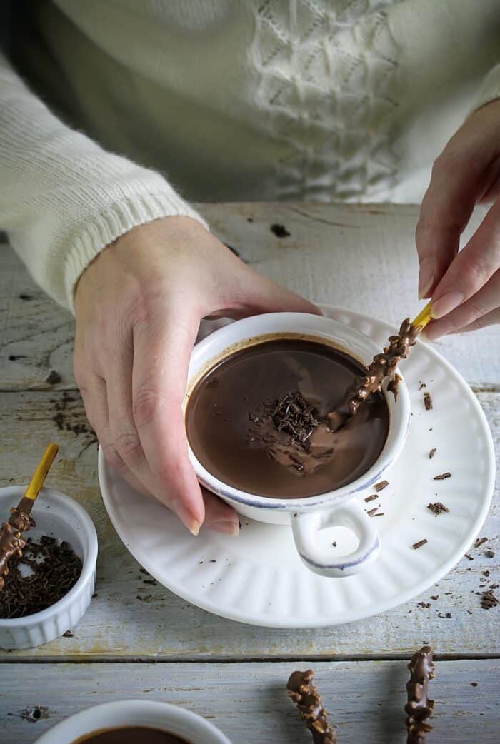 A hand holding the mug of hot chocolate and dipping chocolate stick.