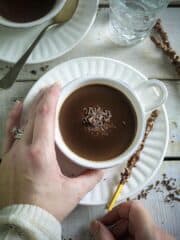 White cups with hot cocoa and saucers on a white wooden surface.