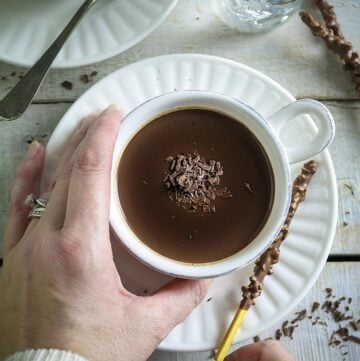 White cups with hot cocoa and saucers on a white wooden surface.