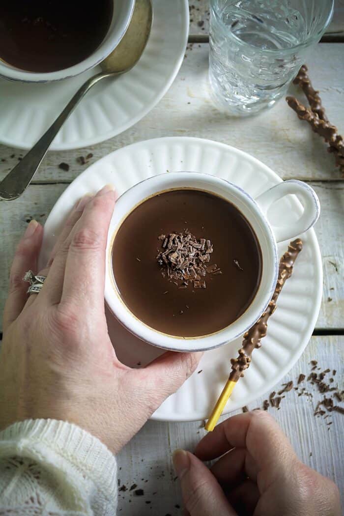 White cups with hot cocoa and saucers on a white wooden surface.