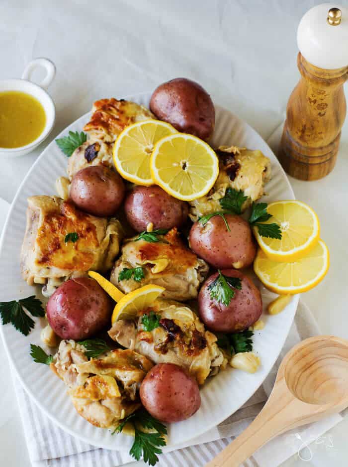 An oval plate with chicken, potatoes, and lemons siting on the white table cloth