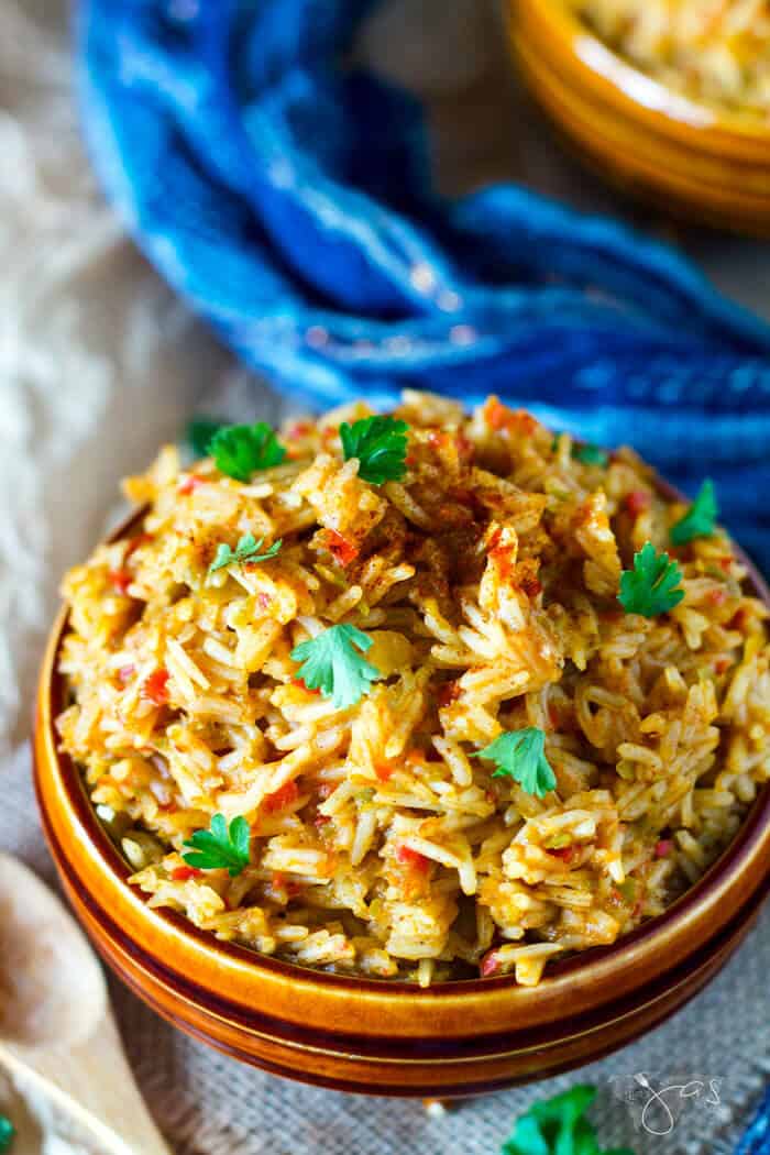 Overhead shot of West African rice dish in a bowl with a blue towel on the side.