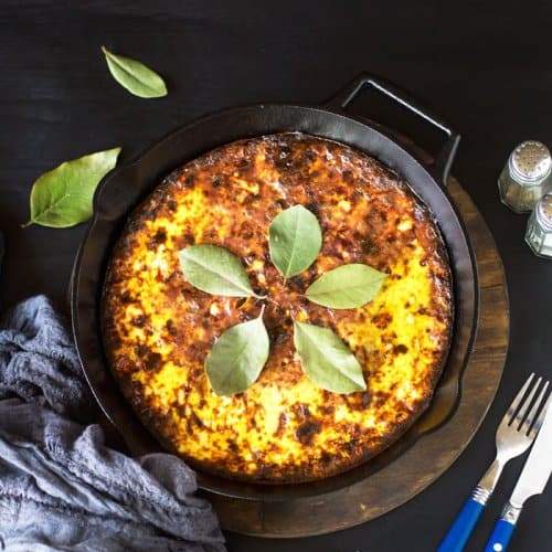 Bobotie in a cast-iron skillet on a black background.