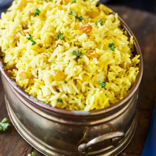 South African sultana yellow rice in an oval copper dish on a wooden trivet.