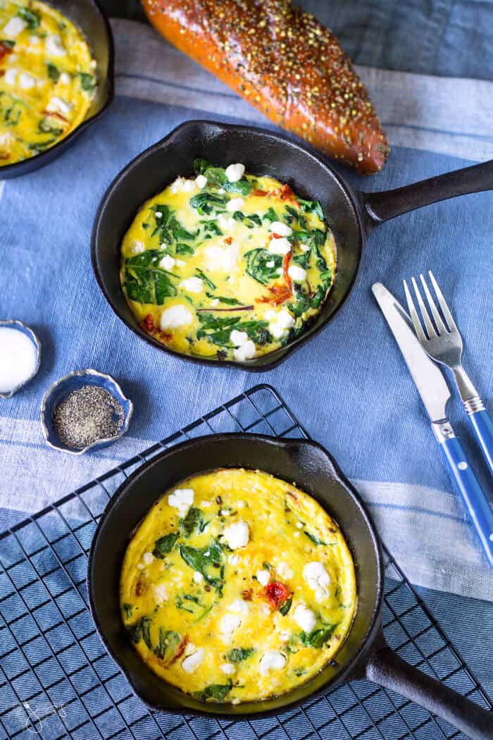 Three mini cast-iron skillets with frittata and bread on a blue tablecloth.