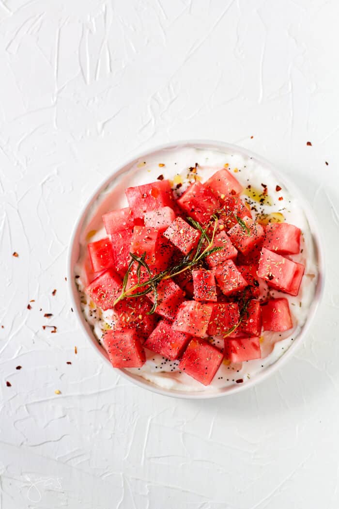 Overhead shot of watermelon salad on a white plate and white background.