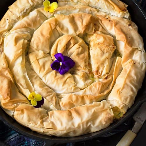 A shot of the Greek style spiral phyllo pie with zucchini in a cast-iron skillet on a black background.