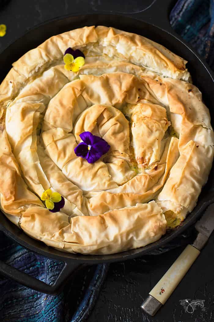 A shot of the Greek style spiral phyllo pie with zucchini in a cast-iron skillet on a black background.