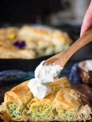 Front shot of the pie slice with layers of shredded zucchini and ricotta cheese, being topped with sour cream.