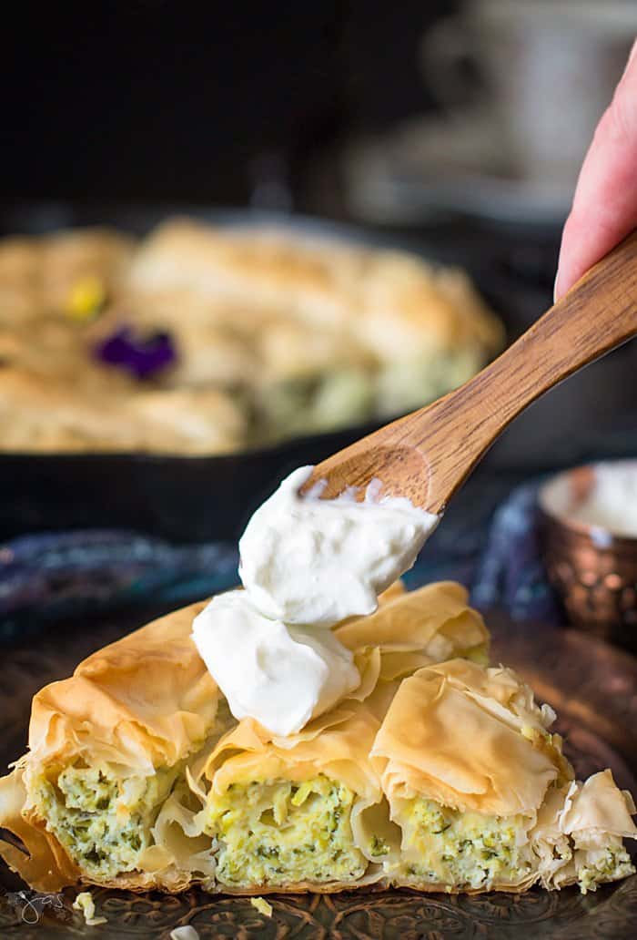 Front shot of the pie slice with layers of shredded zucchini and ricotta cheese, being topped with sour cream.