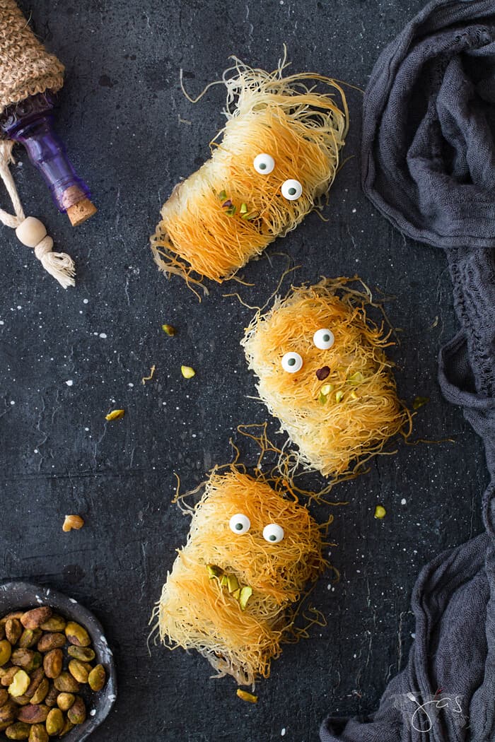 An overhead shot of three Fuzzy and mummy looking kataifi monsters on a black background