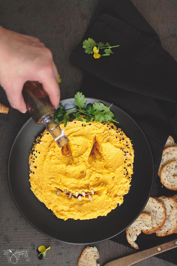 Drizzling olive oil over pumpkin dip Halloween "face".