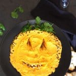 A flat Lay of Halloween Pumpkin Hummus Dip on a black towel and background.