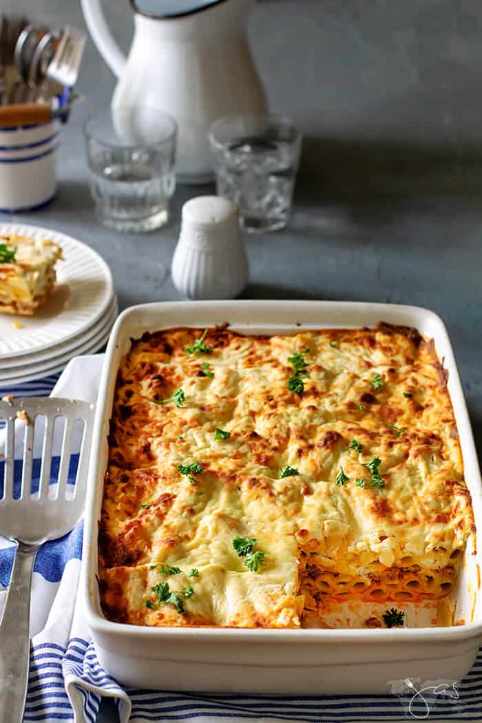 White casserole baking dish with Greek lasagna inside with one square serving removed