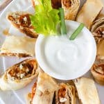 An overhead shot of fillo turnovers on a white plate with a bowl of ranch dressing in the middle