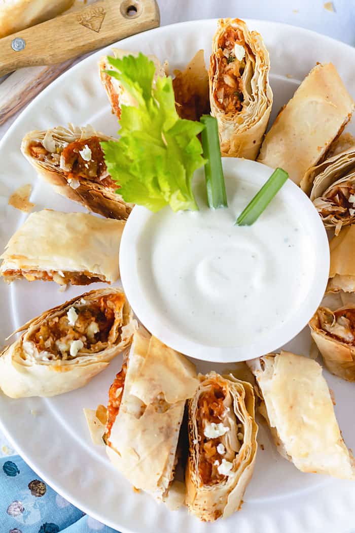 An overhead shot of fillo turnovers on a white plate with a bowl of ranch dressing in the middle