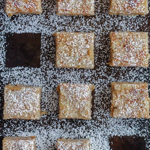 a flat lay of apple cake squares dusted with powdered sugar and two pieces removed
