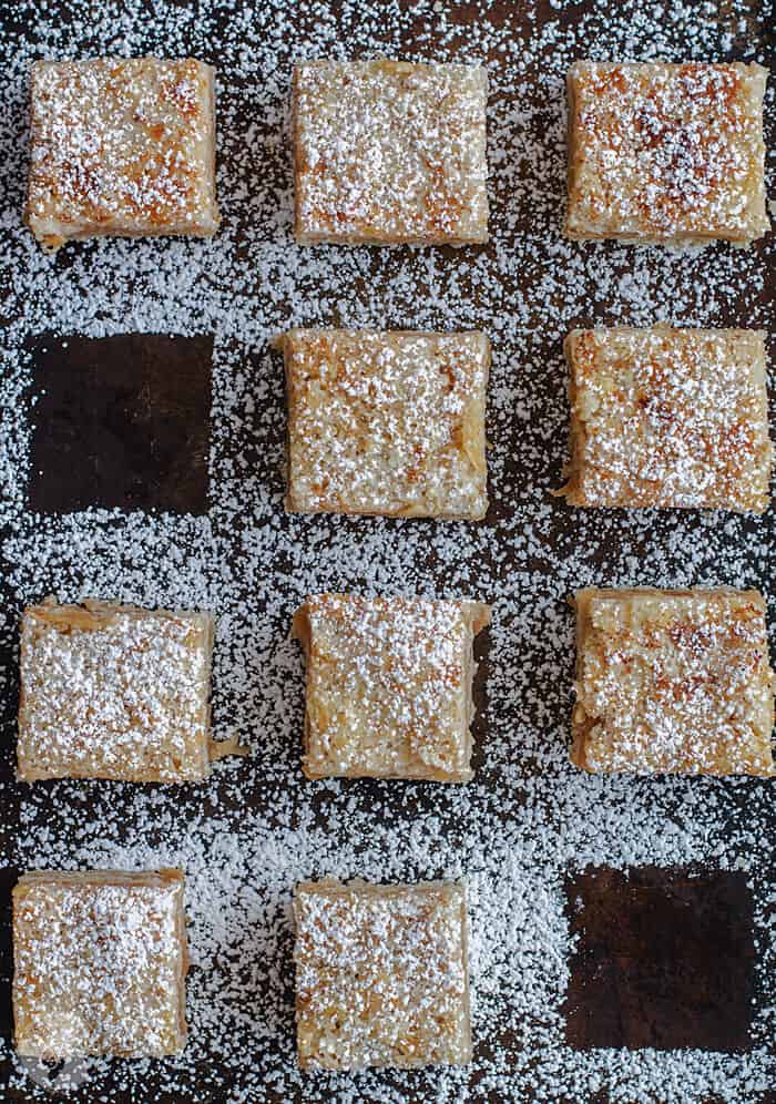 a flat Lay of apple cake squares dusted with powdered sugar and two pieces removed