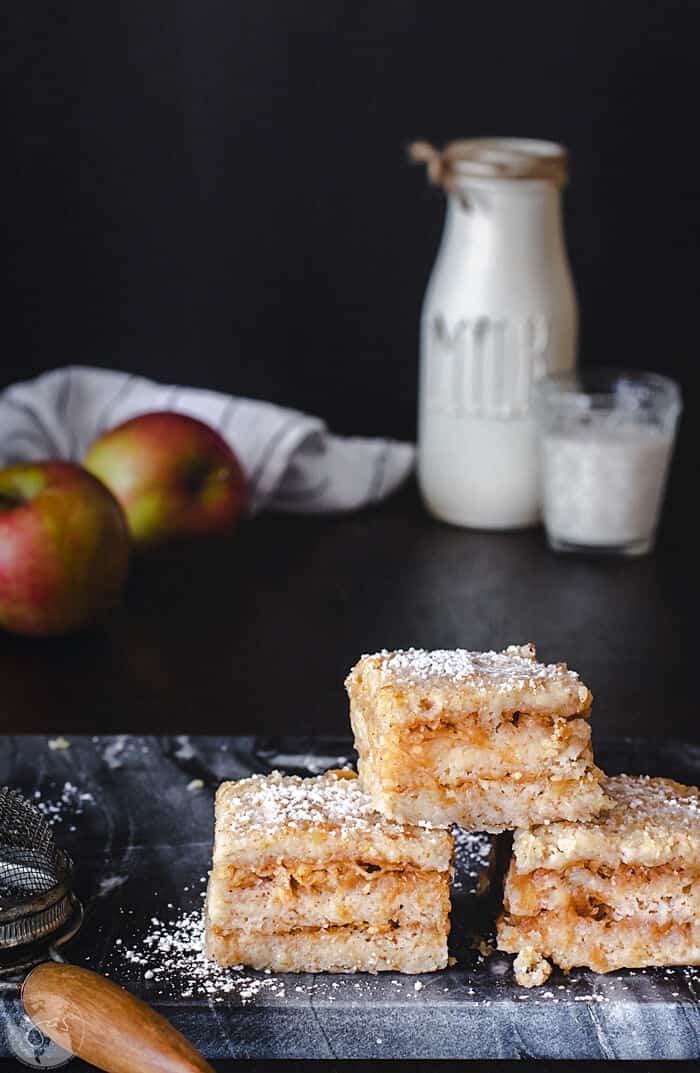 A front shot of three pieces of Croatian apple cake stacked on a with milk bottle and apples in the background