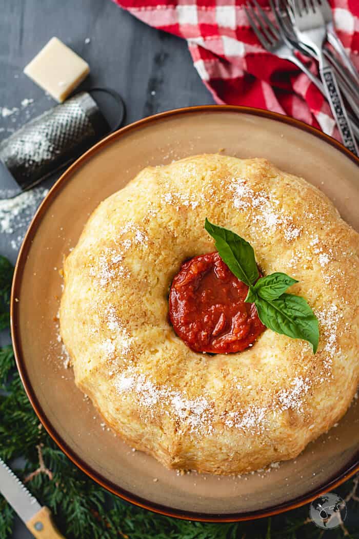 An overhead shot of sartu bundt dish with tomato sauce and basil leaves in the middle on a dark background with red towel.