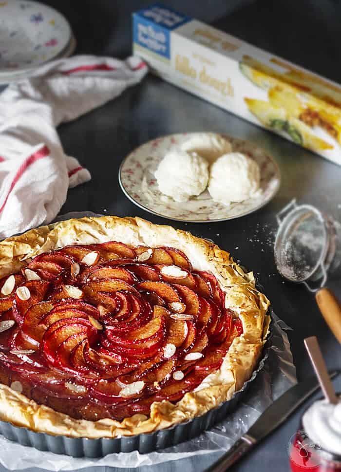 A shot of freshly baked fillo plum pie with ice cream scoops in the background.